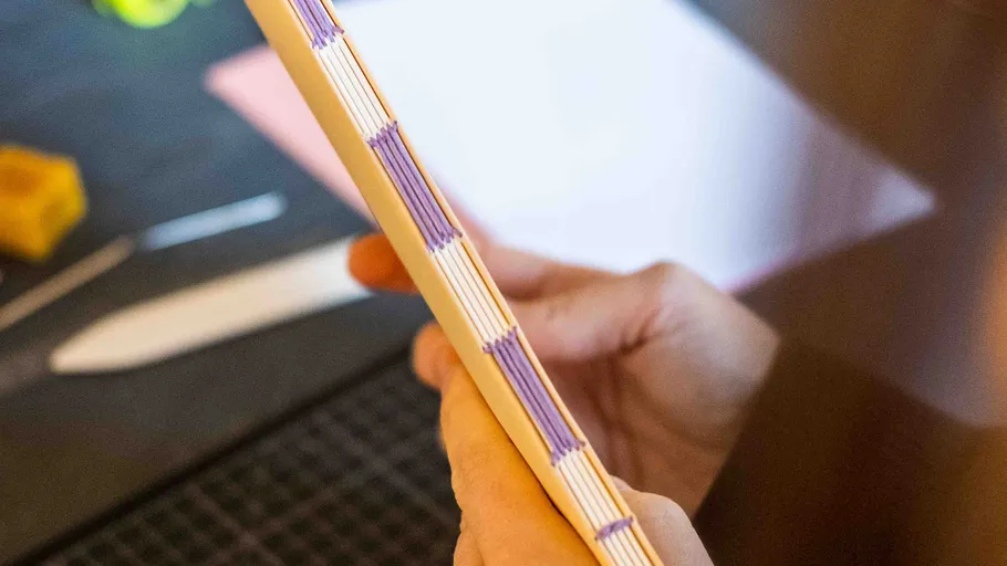 Hand hält genähtes Buchbinden auf Tisch.
