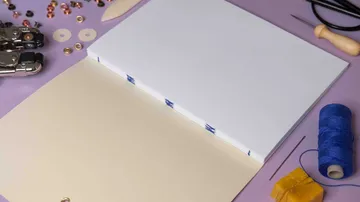 Open notebook with blue thread binding, tools around.