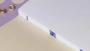 Stack of paper with blue binding, on purple surface.