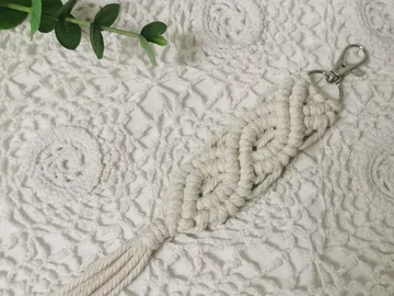 Macrame keychain is placed on a white fabric background.