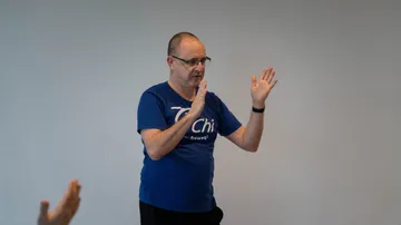 Man practicing Tai Chi indoors, gray background.