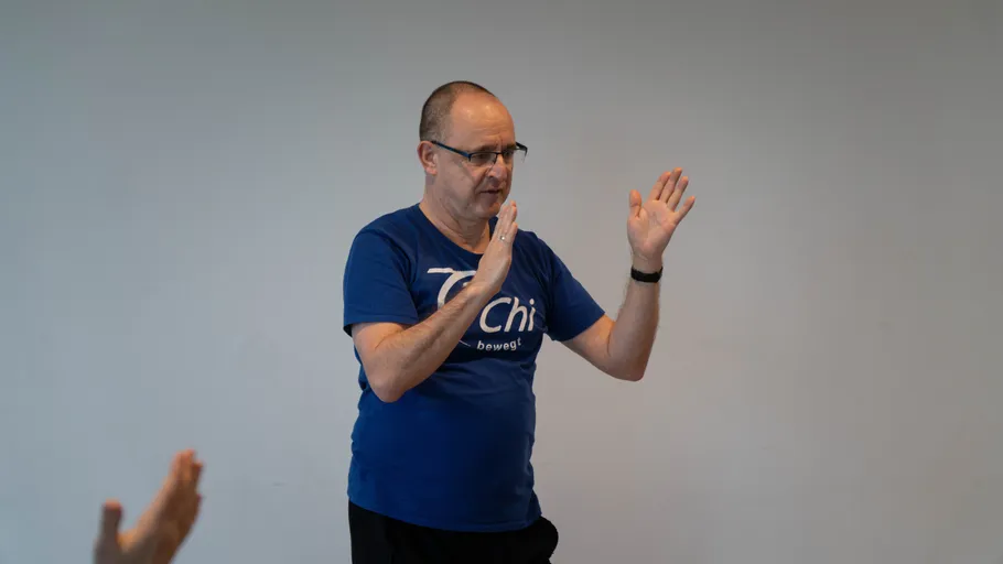 Mann übt Tai Chi drinnen, grauer Hintergrund.