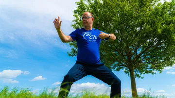 Man practicing Tai Chi outdoors under tree.