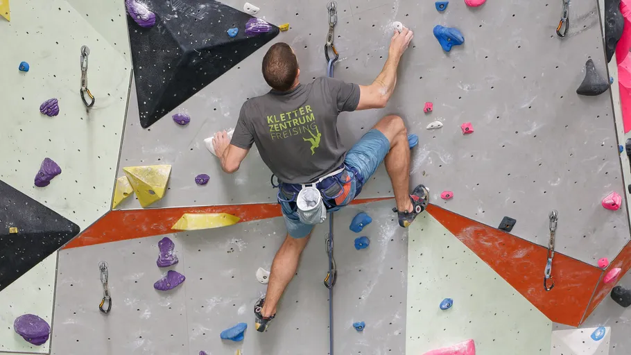 Mann klettert an Kletterwand mit Ausrüstung.