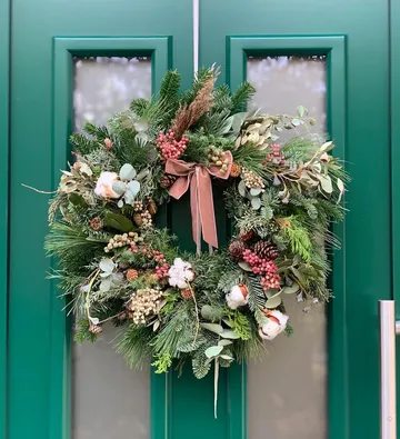 Decorative wreath hanging on green double doors.