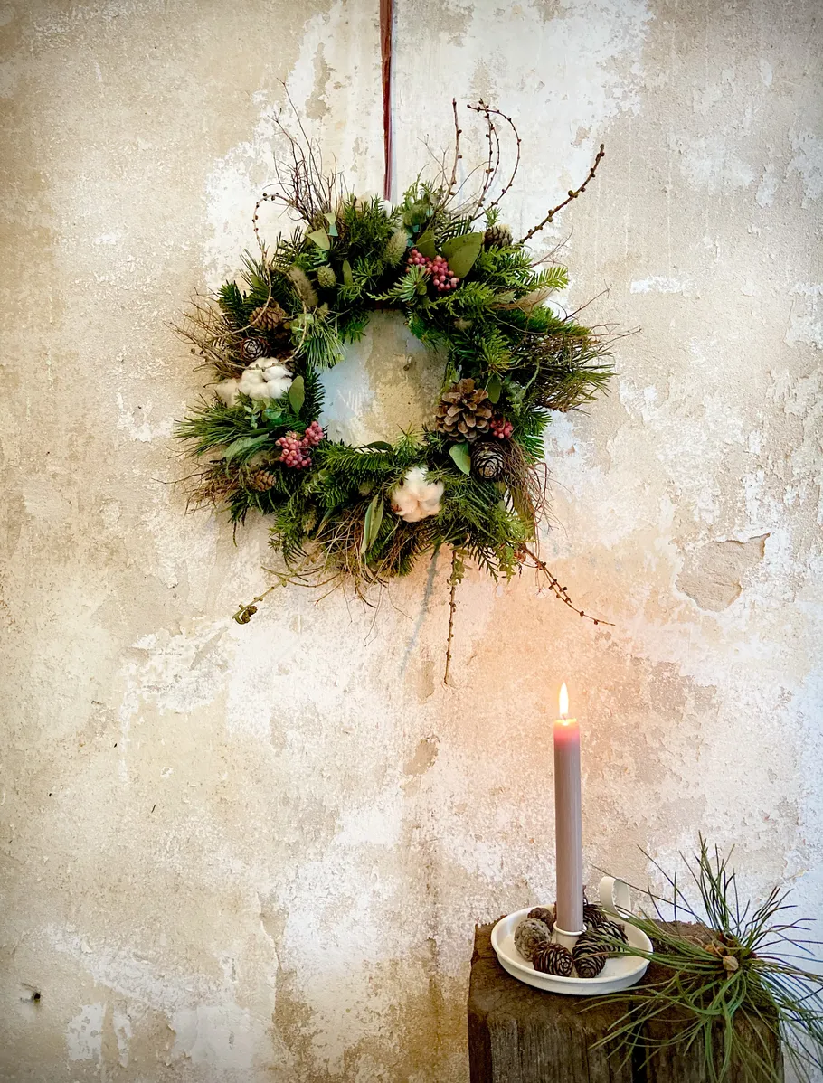 Wreath hanging on textured wall, candle nearby.