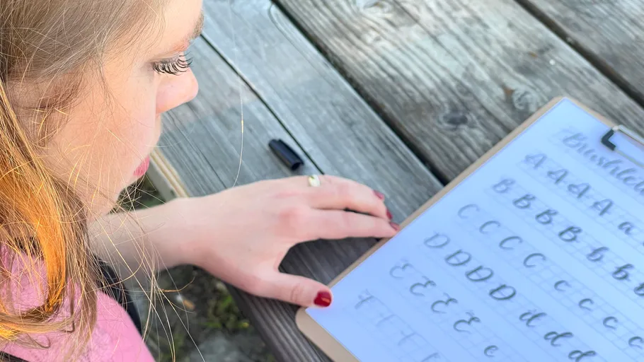 Person practicing calligraphy outdoors at picnic table.