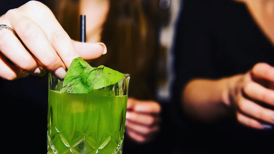 Person verziert grünen Cocktail mit Blatt.