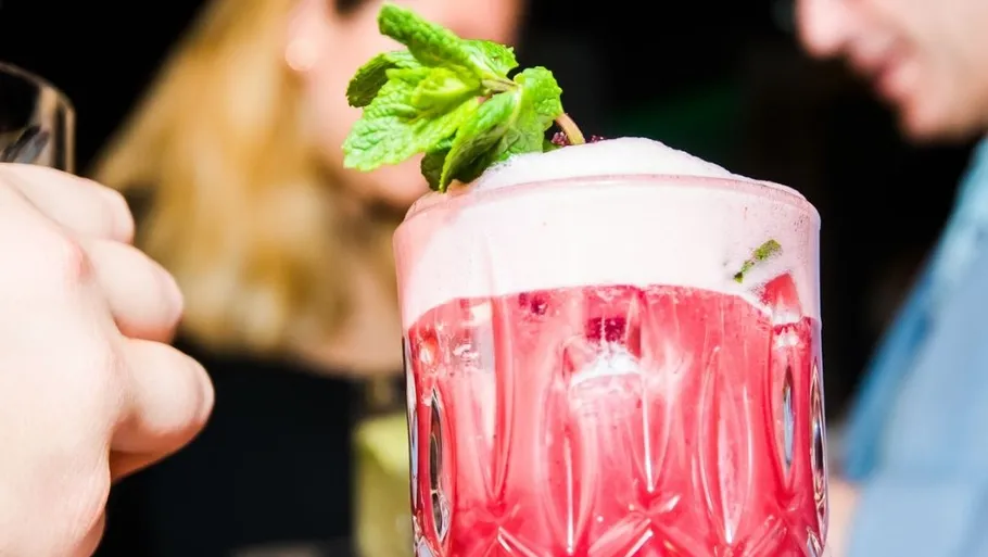 Pink cocktail with mint garnish at party.