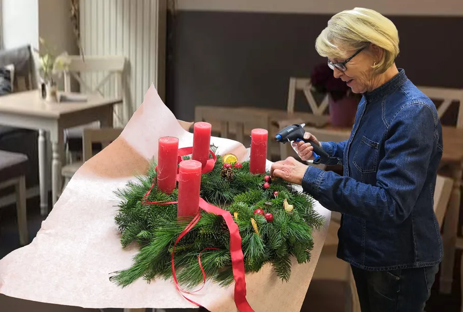 Woman decorating wreath with candles in room.