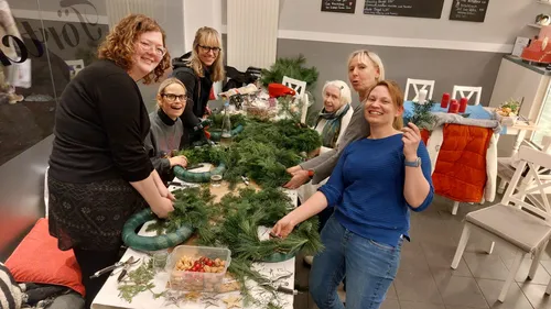 Women crafting wreaths at a table indoors.