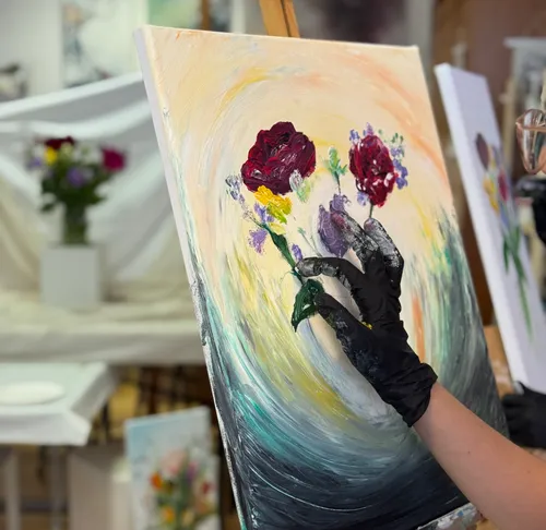 Behandschuhte Hand malt Blumen auf Leinwand.