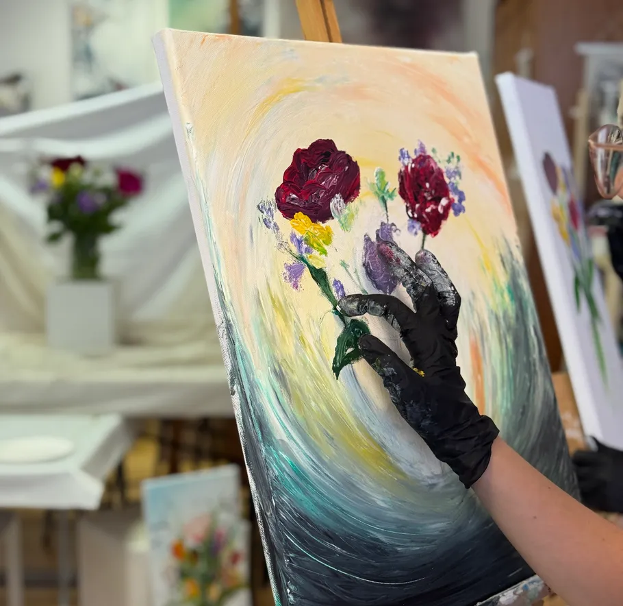 Gloved hand painting flowers on canvas.