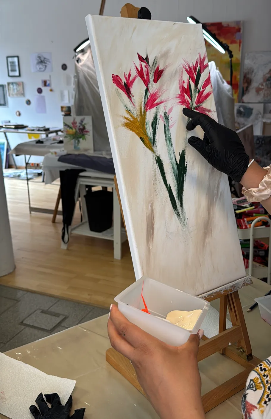 Person painting flowers on canvas in studio.