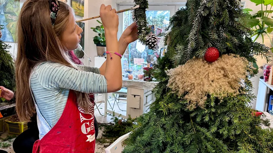 Girl decorating tree-shaped festive arrangement indoors.