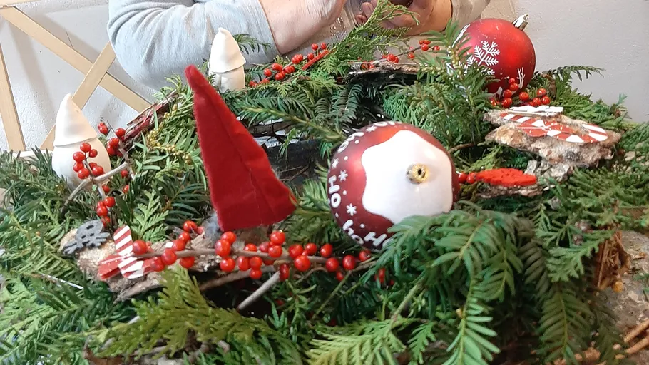 Holiday wreath being decorated on table.