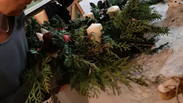 Person crafting a wreath with candles indoors.