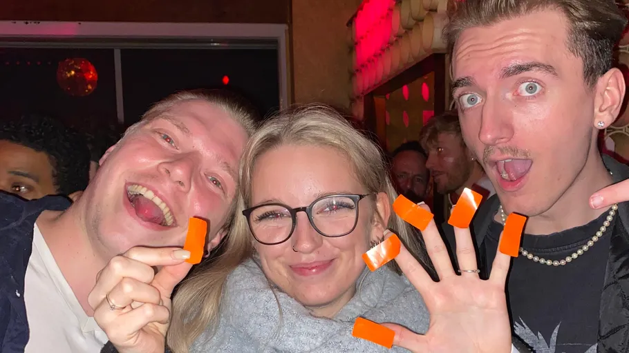 Drei Personen halten orange Streifen in einer Bar.