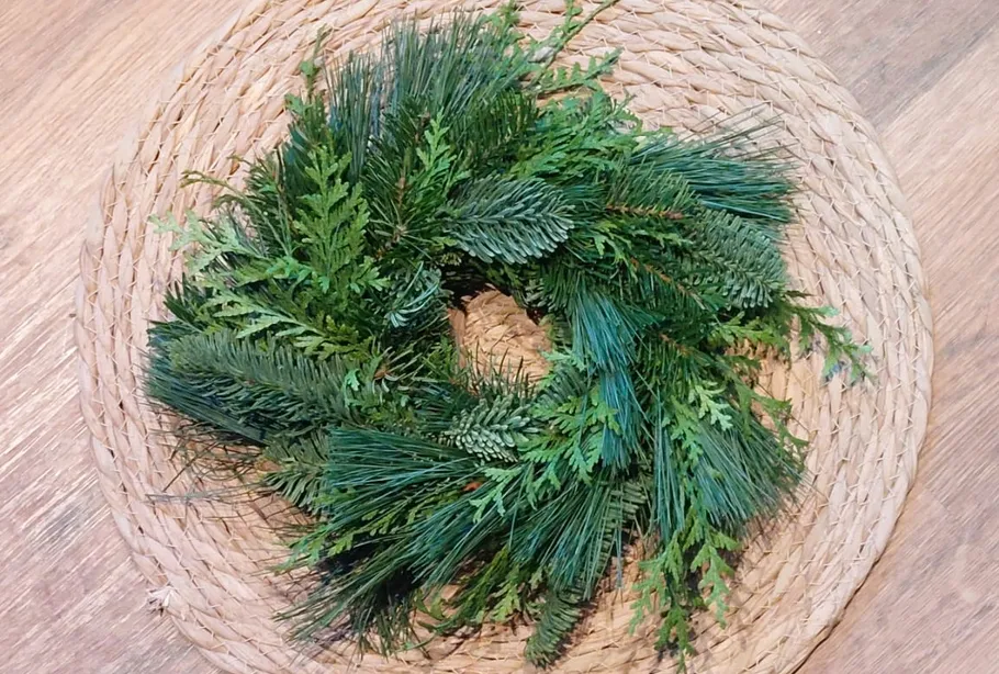 Grüner Kranz auf geflochtener Matte, Holztisch.