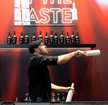 Barkeeper jongliert Flaschen vor Regalen.