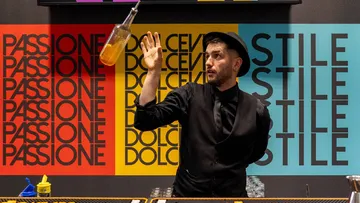 Barkeeper wirft Flasche vor bunter Wand.