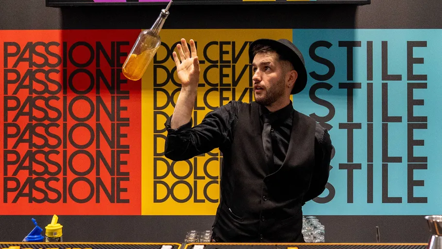 Barkeeper wirft Flasche vor bunter Wand.