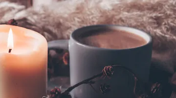 Candle and coffee mug on cozy background.