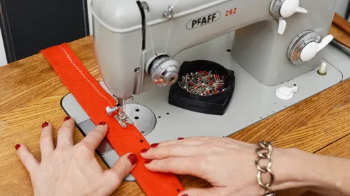 Hands sewing red fabric on Pfaff machine.