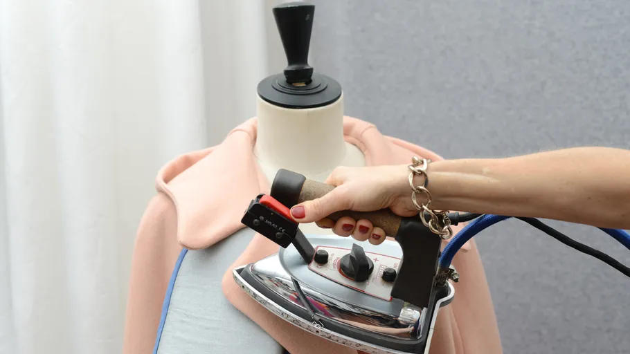 Hand bügelt rosa Stoff auf einer Puppe.