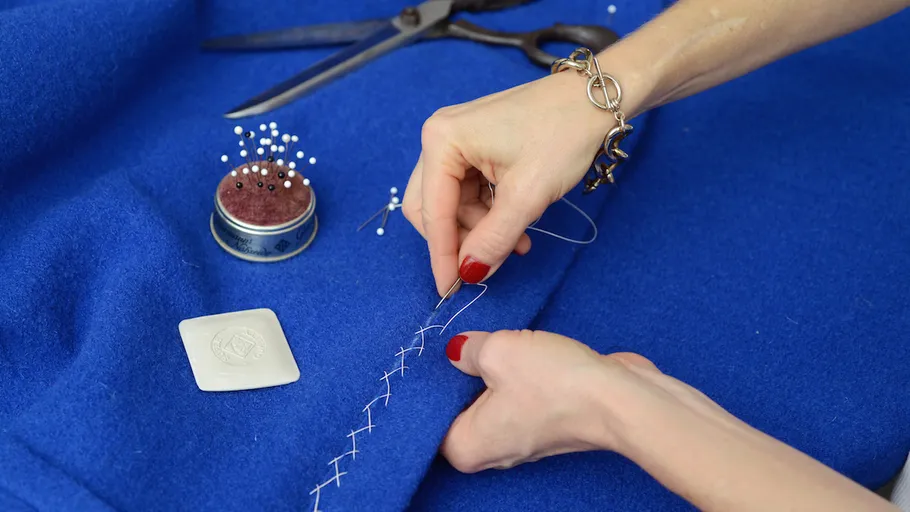 Hands stitching blue fabric with needle.