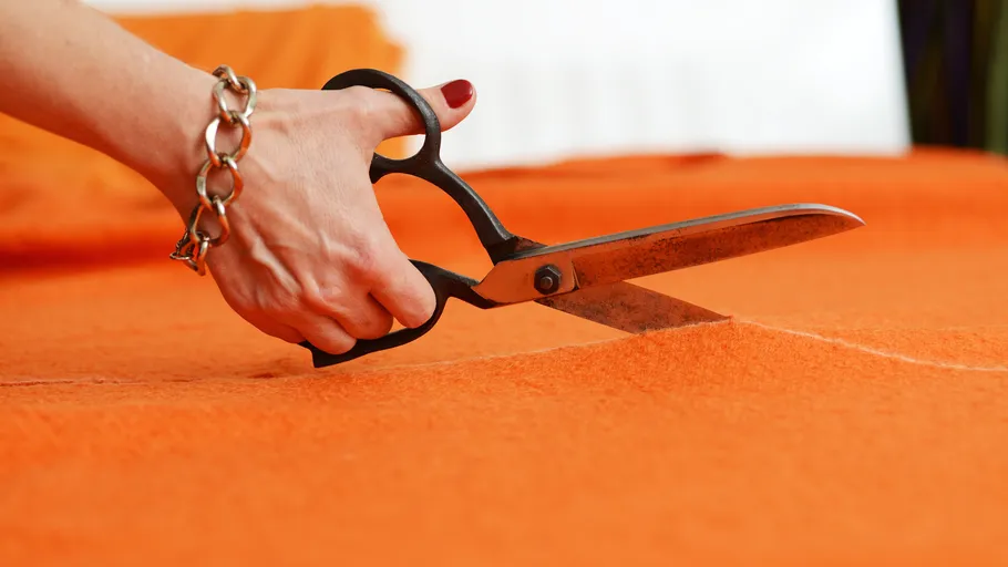 Hand schneidet orange Stoff mit Schere.