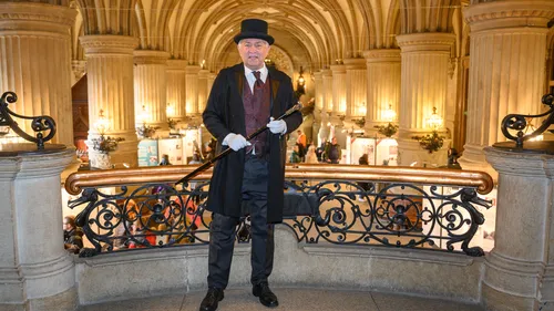 Man in vintage attire stands in ornate hall.
