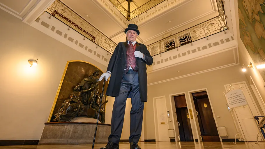 Man in vintage attire with cane, elegant building.