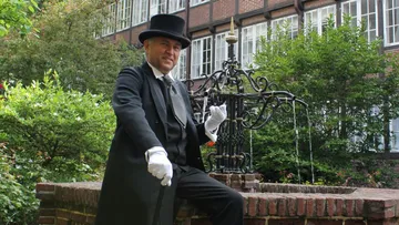 Mann in formeller Kleidung sitzt am Brunnen.
