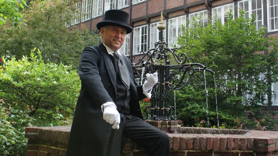 Man in formal attire sits near decorative fountain.