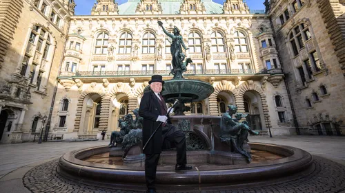 Man in formal attire by historic fountain.