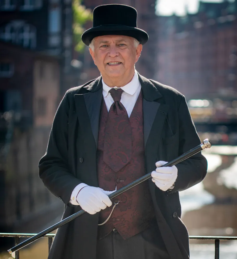 Man in vintage attire holds a cane outside.