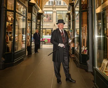Man in formal attire with cane in arcade.