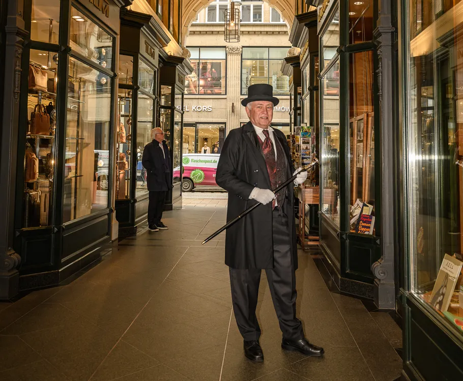 Mann in formeller Kleidung mit Stock in Arkade.