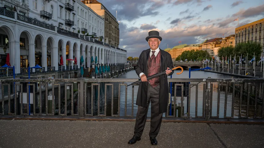 Man in historical attire with umbrella by canal.