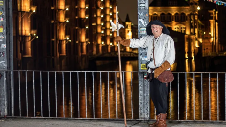 Person in historical attire holds staff by canal.