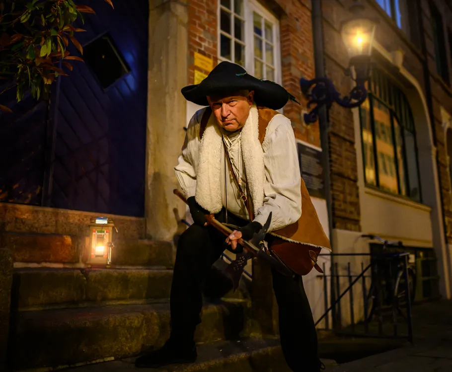 Man in historical costume crouches by building steps.