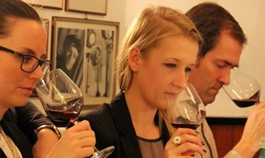 Drei Personen riechen an Rotwein in Gläsern.