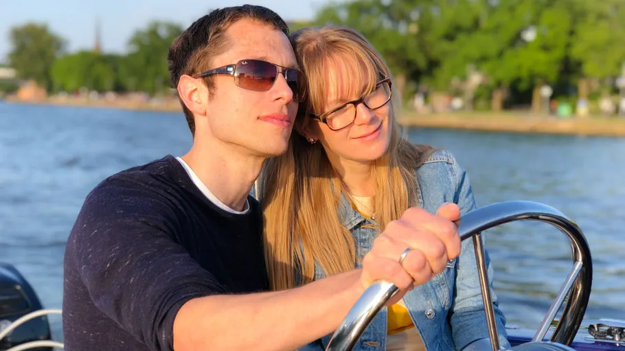 Couple steering a boat on calm water.