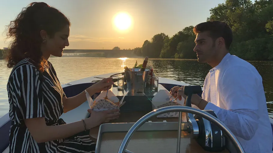 Two people dining on a boat at sunset.