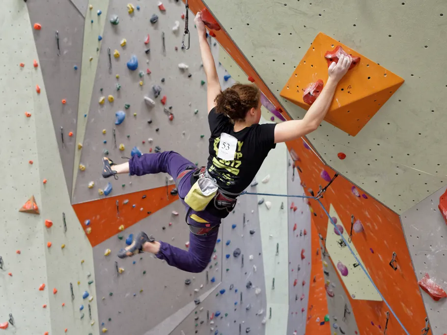 Climber hanging on colorful indoor wall.