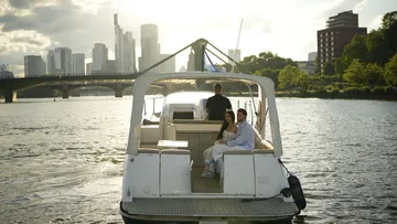 Yacht fährt auf Fluss, Stadtansicht im Hintergrund.