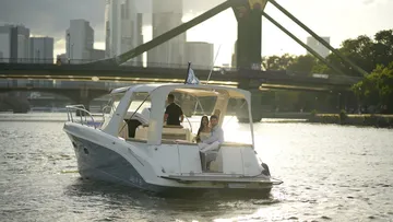 Motorboot mit Menschen fährt nahe Stadtbrücke.