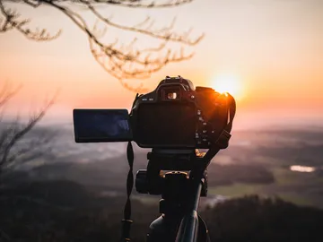 Camera on tripod photographs sunset over landscape.