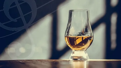 Whiskey glass on wooden table, shadowy background.